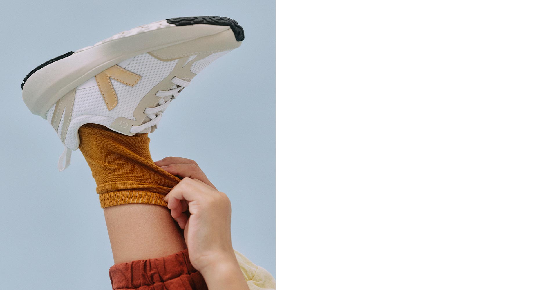 Un bambino che tiene in mano i suoi calzini color ocra, con scarpe da ginnastica di platino bianco canarino