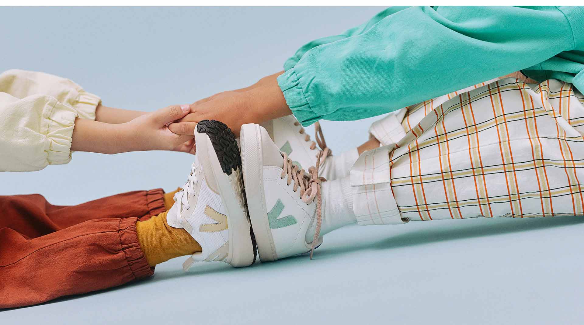 Focus on the hands of two children wearing Veja trainers