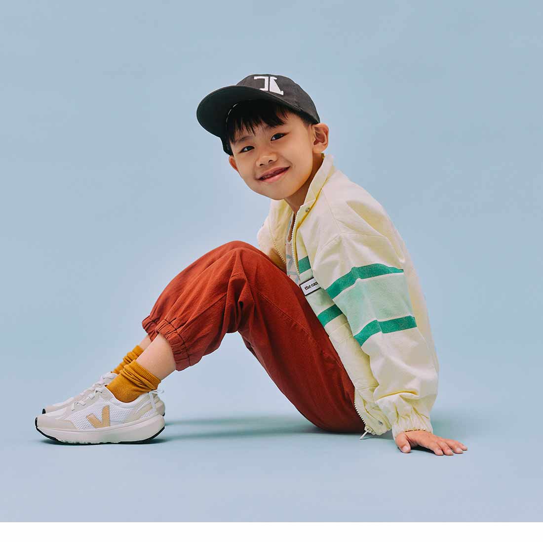Child sitting dressed in a streetwear outfit and wearing Veja canary alveomesh white platinum shoes