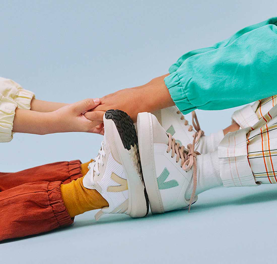 Focus on the hands of two children wearing Veja trainers