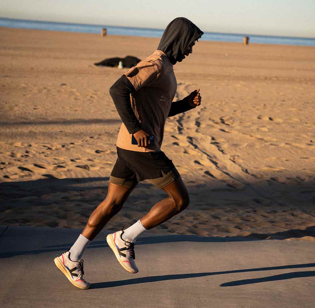 Man with a hoodie running along the beach